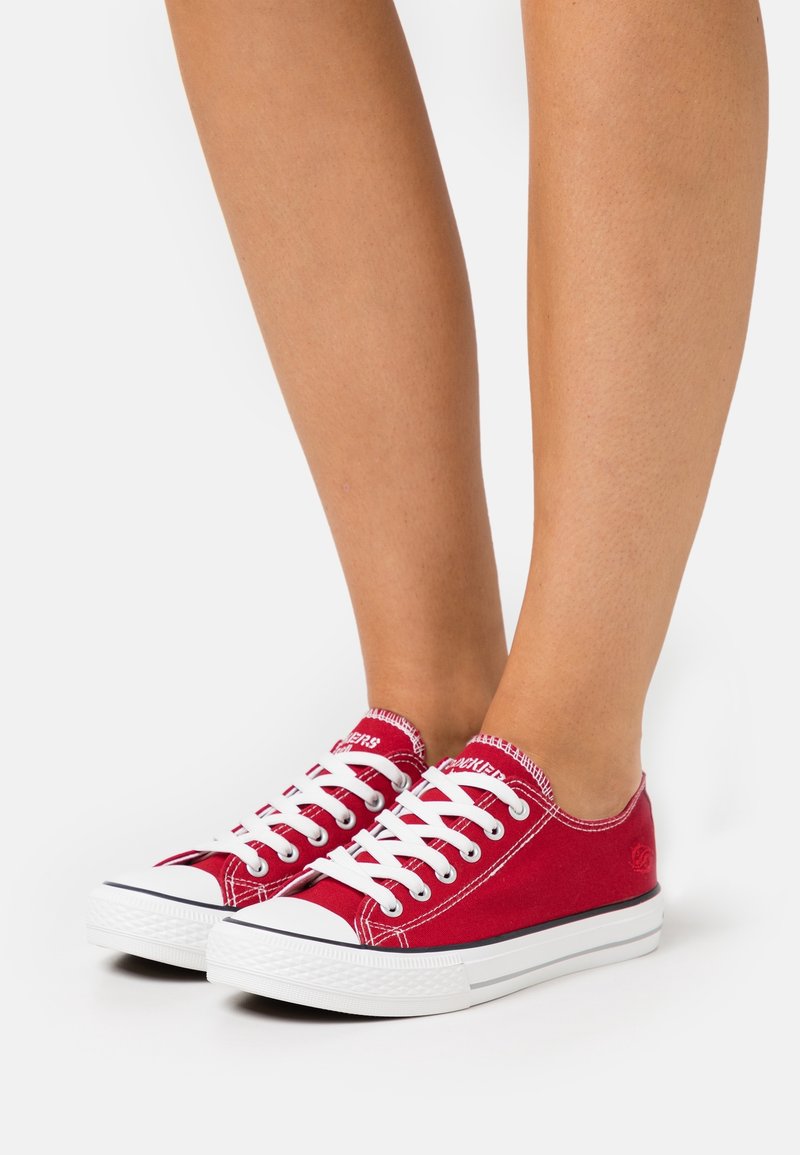 Sneaker in tela rossa con lacci bianchi, punta rotonda e suola in gomma. Include cuciture a contrasto e dettaglio del logo sul lato.