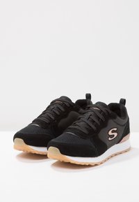 Schwarze Sportschuhe aus Mesh und Wildleder, mit einer weißen Zwischensohle, einer Gummisohle und einem roségoldenen Akzent an der Seite.