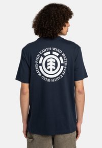 Marineblaue Baumwoll-T-Shirt mit einem kreisförmigen weißen Grafik, die den Text "Wasser, Erde, Wind, Feuer" und ein zentrales Logo auf der Rückseite zeigt.