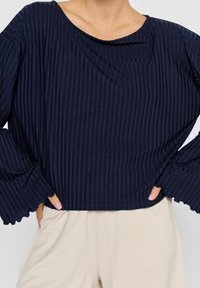 Navyblauwe geribbelde lange mouwen top met een ronde halslijn en wijde mouwen. Textuurstof met een licht glanzende afwerking. Cropped ontwerp.