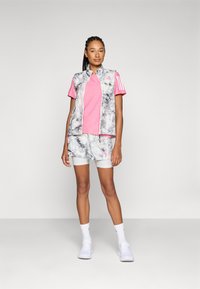 Conjunto deportivo que incluye una camiseta rosa, una chaqueta sin mangas de estampado mármol gris y pantalones cortos a juego con detalles blancos y calcetines.