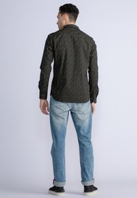 Camisa negra con un patrón sutil, de manga larga y con cuello abotonado, combinada con jeans de lavado claro y zapatillas negras.