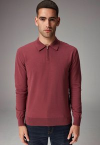 Maronfarvet langærmet polo skjorte med lynl�ås i halsen, ribbede manchetter og søm, med en glat strikket tekstur. Båret over mørke jeans.