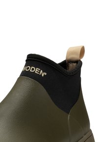 Bottines vert olive avec une semelle en caoutchouc texturé, tige en tissu noir et une languette beige à l'arrière. Présente un logo de marque discret.
