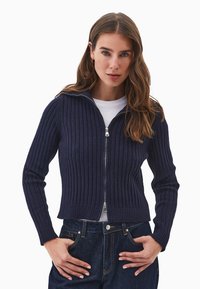 Tumman sininen ribbikuvioinen zip-up villapaita pitkillä hihoilla ja istuvalla siluetilla, varustettuna metalliketjulla ja sileällä sisäpinnalla.