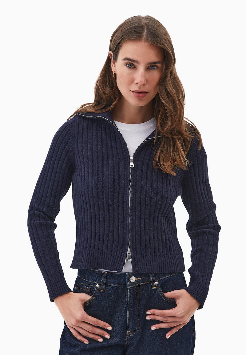 Tumman sininen ribbikuvioinen zip-up villapaita pitkillä hihoilla ja istuvalla siluetilla, varustettuna metalliketjulla ja sileällä sisäpinnalla.