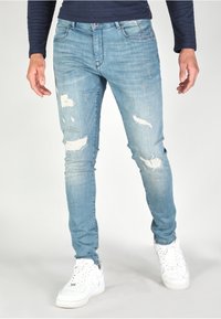 Ljusblå slitna jeans med rivningar, figurnära design och en lätt stretch. Kombineras med vita sneakers för en avslappnad look.