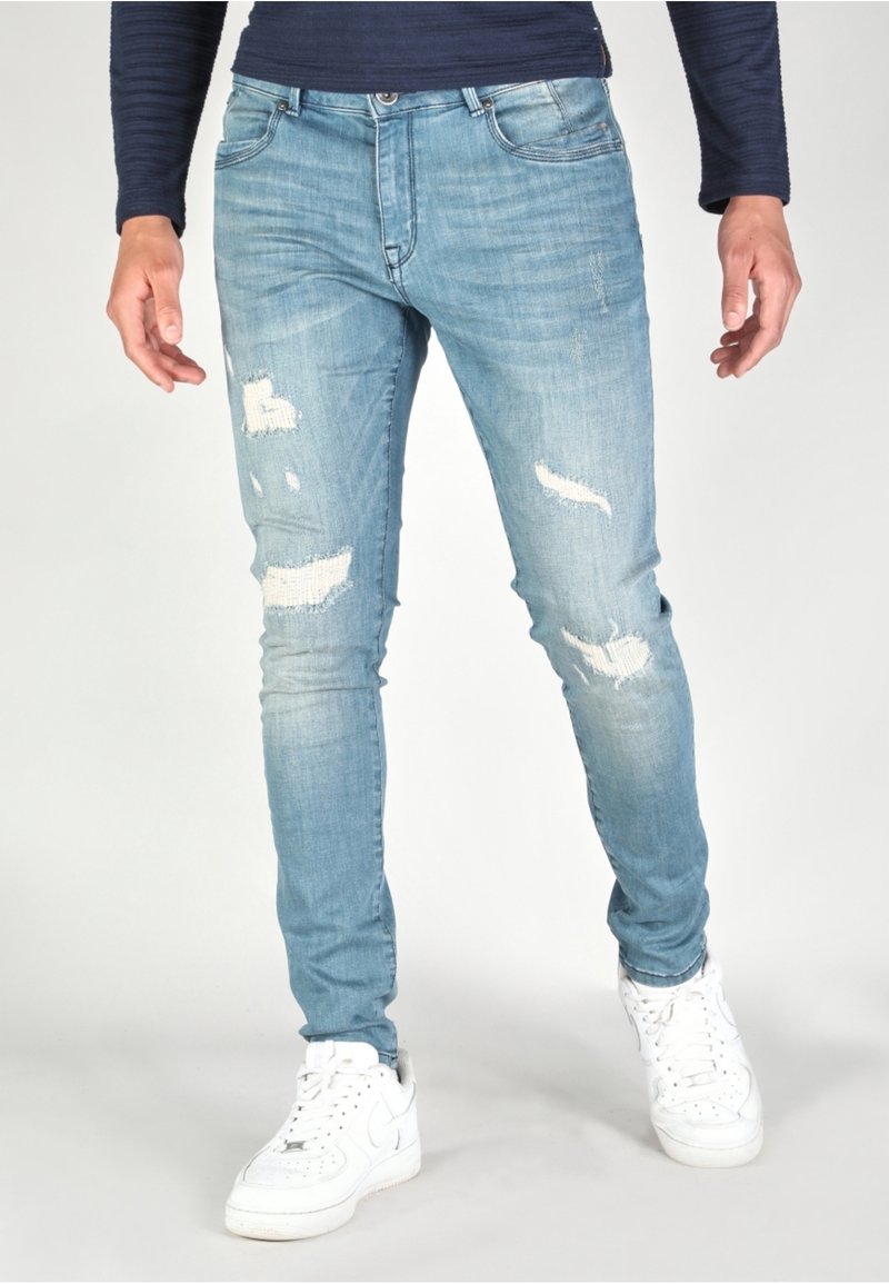 Ljusblå slitna jeans med rivningar, figurnära design och en lätt stretch. Kombineras med vita sneakers för en avslappnad look.
