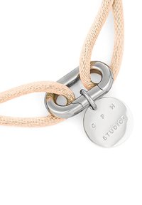 Una chiusura in metallo argentato collega un cordone intrecciato rosa testurizzato, che presenta una targhetta circolare con la scritta in rilievo "C P H STUDIOS."