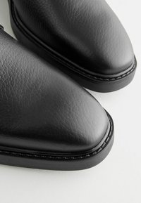 Chaussures en cuir noir avec une finition texturée, bouts ronds et semelle contrastée cousue. Des bords lisses rehaussent le design élégant.