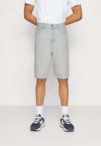 Svetle modré denimové šortky s rovný střih, vybavené pěti kapsami a zapínáním na knoflík. Kombinované s bílými ponožkami a tmavými teniskami.