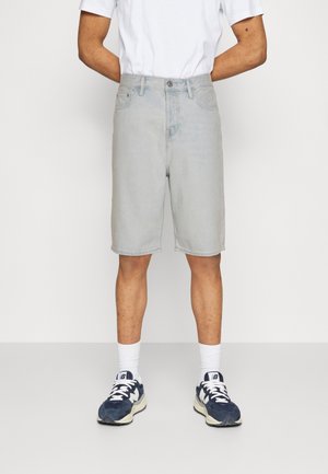 Shorts en denim bleu clair à coupe droite, avec cinq poches et une fermeture à boutons. Associés à des chaussettes blanches et des baskets noires.