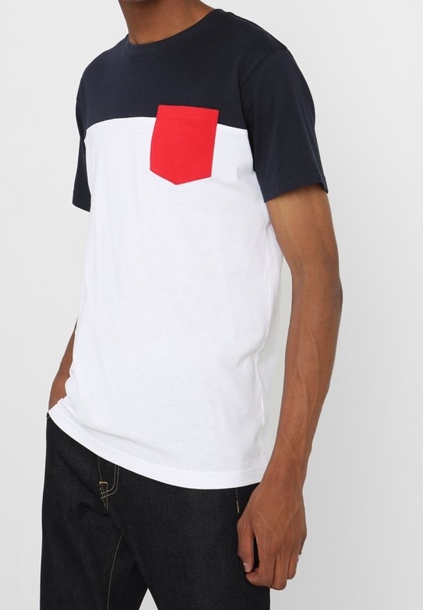 Homme portant un t-shirt à manches courtes bicolore avec le haut bleu marine, le bas blanc et une poche poitrine rouge, associé à un jean foncé.