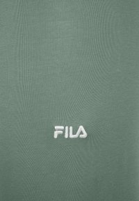 Groene katoenstof met een gladde textuur, voorzien van een witte geborduurde "FILA"-logo in de rechteronderhoek.
