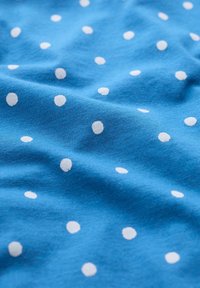 Blått tyg med en mjuk struktur, som har jämnt fördelade, vita prickar i olika storlekar på en slät yta.