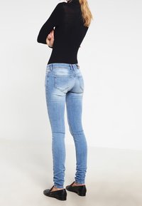 Vaqueros ajustados en denim de color azul claro con un lavado desgastado, que presentan una cintura de altura media, diseño de cinco bolsillos y una textura suave.