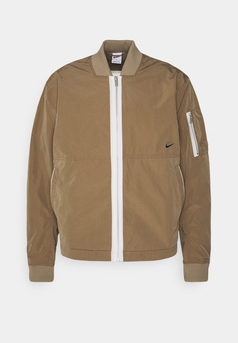 Brown bomber jacket with a white front zipper, ribbed cuffs, and a zippered sleeve pocket. Features a black Nike logo on the chest.