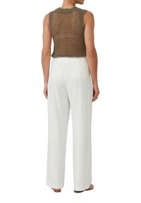 Top senza maniche di un verde oliva a maglia con un design a trama aperta, abbinato a pantaloni bianchi a vita alta con tasche posteriori.