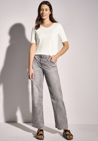 Haut blanc à manches courtes avec un col en V, associé à un jean large gris pâle, et des sandales noires avec des accents en métal doré.