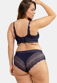 Ensemble de lingerie bleu marine avec détails en dentelle. Le soutien-gorge présente des bretelles larges et des bords festonnés ; le culotte assortie a une insert en dentelle à l'arrière.