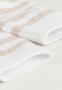Pasiaste skarpetki wykonane z miękkiego materiału w białym i jasnobeżowym kolorze, z prążkowanymi ściągaczami i puszystą teksturą dla komfortu i ciepła.