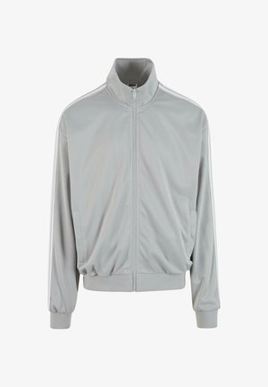 Pilkas sportinis džemperis su aukštu kaklu, užtrauktuku, banguotomis rankovėmis ir kontrastingomis baltomis juostomis palei pečius. Lietaus, lengvas audinys.