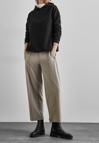 Sweat-shirt à capuche noir avec motif en losanges texturé, associé à un pantalon large beige clair avec galon latéral. Bottines noires pour compléter le look.