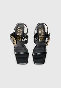 Black leather high-heel sandals with a square toe, featuring thin straps and a gold-tone buckle detail on the ankle strap.
