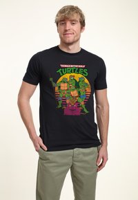 T-shirt nera a maniche corte con stampa grafica colorata di tartarughe dei cartoni animati su uno sfondo sfumato. Tessuto morbido, vestibilità casual.
