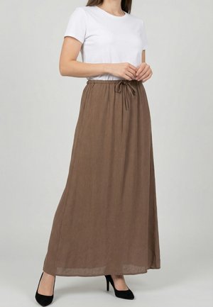 Donna che indossa una camicia bianca a maniche corte infilata in una gonna marrone lunga fino alla caviglia con coulisse in vita, abbinata a tacchi alti neri.