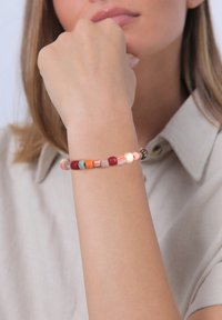 Bracciale di perline con colori assortiti tra cui rosa, rosso, verde e arancione, con forme e texture diverse. Indossato su un polso.
