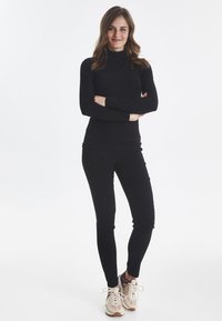 Sort langærmet top parret med sorte tætsiddende bukser, båret med lyse sneakers. Enkel design med en glat, strækbar tekstur.