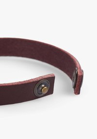 Pulsera de cuero burdeos con una textura suave y un cierre de broche que presenta un acento de botón de bronce. Diseño plano y minimalista.