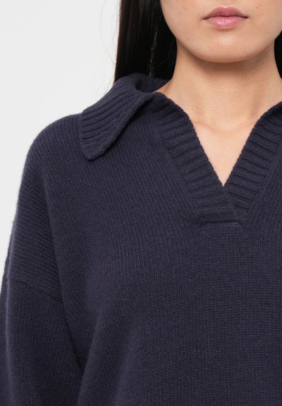 Navy blue knit sweater with a ribbed collar and V-neck design. Soft texture, oversized fit, showcasing horizontal and vertical knit patterns.