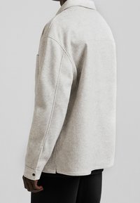 Szara kurtka z mieszanki wełny o luźnym kroju, z kołnierzem w szpic, bocznymi kieszeniami i mankietami na guziki. Teksturowany materiał o miękkim wykończeniu.