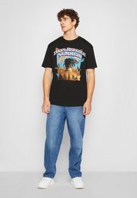 Black cotton t-shirt featuring a colorful graphic design with the phrase "DAYS BEFORE SUMMER," set against a nature background and butterflies.