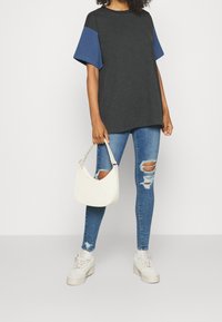 Camiseta negra de gran tamaño con mangas cortas azules, combinada con jeans skinny azules desgastados y un bolso blanco. Zapatillas de plataforma blancas.