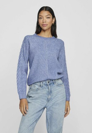 Maglione azzurro lavorato a maglia con un motivo a diamante testurizzato e maniche con lavorazione a treccia, abbinato a jeans a vita alta in denim chiaro.
