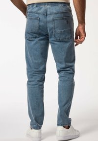 Pantalones jogger de mezclilla azul claro con cintura elástica, dos bolsillos traseros y un corte ajustado. La tela tiene una textura suave.