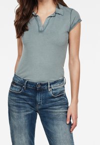 Bodies de color azul claro con cuello y diseño ajustado, combinados con jeans de color azul oscuro deslavados que presentan sutiles detalles de desgaste y bolsillos clásicos.