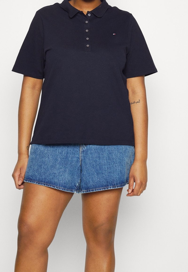Marinblå pikétröja i bomull, med klassisk krage och fyra knappslå. Tillsammans med ljusblå denimshorts.