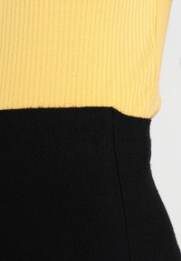 Ribbed sweater featuring a yellow top section and a black bottom section, highlighting a contrasting color block design and soft texture.