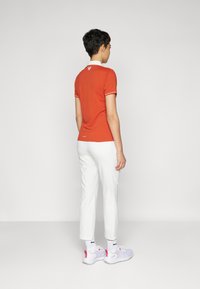 Rotes Polo-Shirt mit weißem Kragen und Manschetten, kombiniert mit weißen Slim-Hosen und hellen Sneakern. Mit einem kleinen Logo auf dem Rücken.