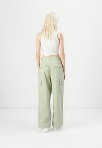 Lichtgroene cargobroek met een comfortabele pasvorm, voorzien van grote zijzakken en een patch op de achterzak. G draagt een witte cropped tanktop.