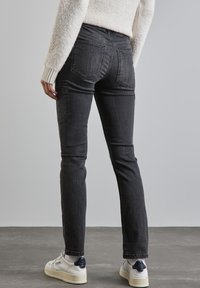 Czarne dżinsy o dopasowanym kroju, z tylnymi kieszeniami i subtelnym przetarciem, w połączeniu z białymi trampkami oraz teksturowanym kremowym swetrem.