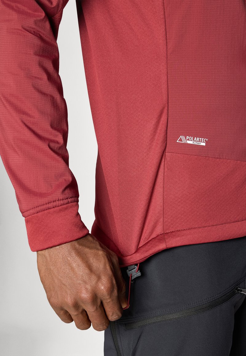 Rode longsleeve shirt gemaakt van gestructureerde stof, met een aansluitende manchette en een zijzak met een trekkoord. Polartec-logo zichtbaar.