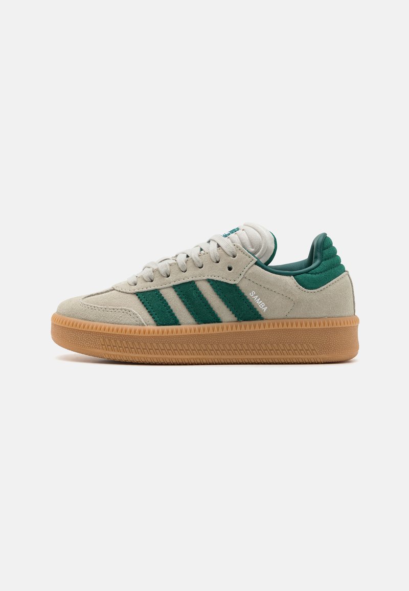 Zapatillas de ante beige claro con rayas y acentos verdes, que cuentan con una suela de goma y un detalle de talón acolchado. Modelo etiquetado como "SAMBA."