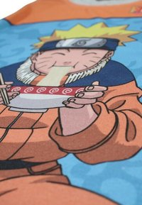 T-shirt à manches courtes avec un graphisme vibrant d'un personnage aux cheveux blonds en pics, tenant un bol de nouilles avec des détails en spirale rouge.