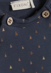 Kruidige blauwe katoenen overhemd met een ronde hals, twee houten knopen en een patroon van kleine, gekleurde driehoeken over de stof.