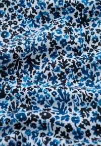 Kukkakuvioinen kangas, jossa on valkoinen tausta ja sinisiä sekä mustia kuvioita. Tekstuuri vaikuttaa pehmeältä ja sillä on hieno kiilto.